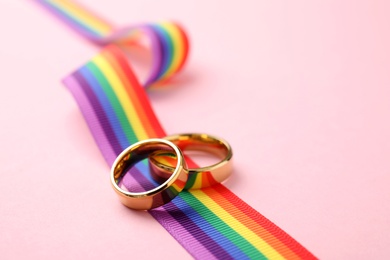 Photo of Wedding rings and rainbow ribbon on color background, space for text. Gay symbol