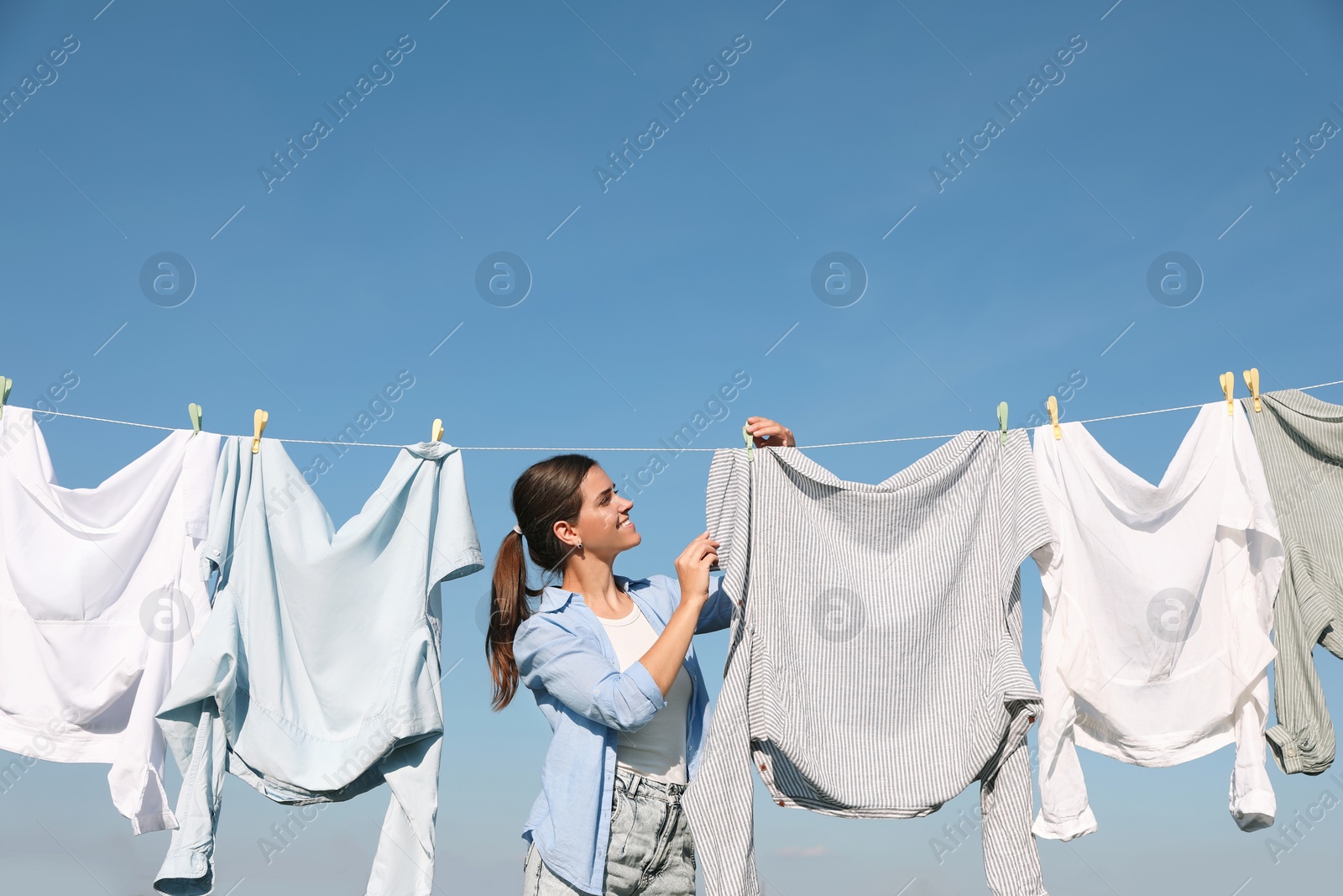 Photo of Woman hanging clothes with clothespins on washing line for drying against blue sky