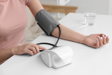 Photo of Woman measuring blood pressure with tonometer at table indoors, closeup