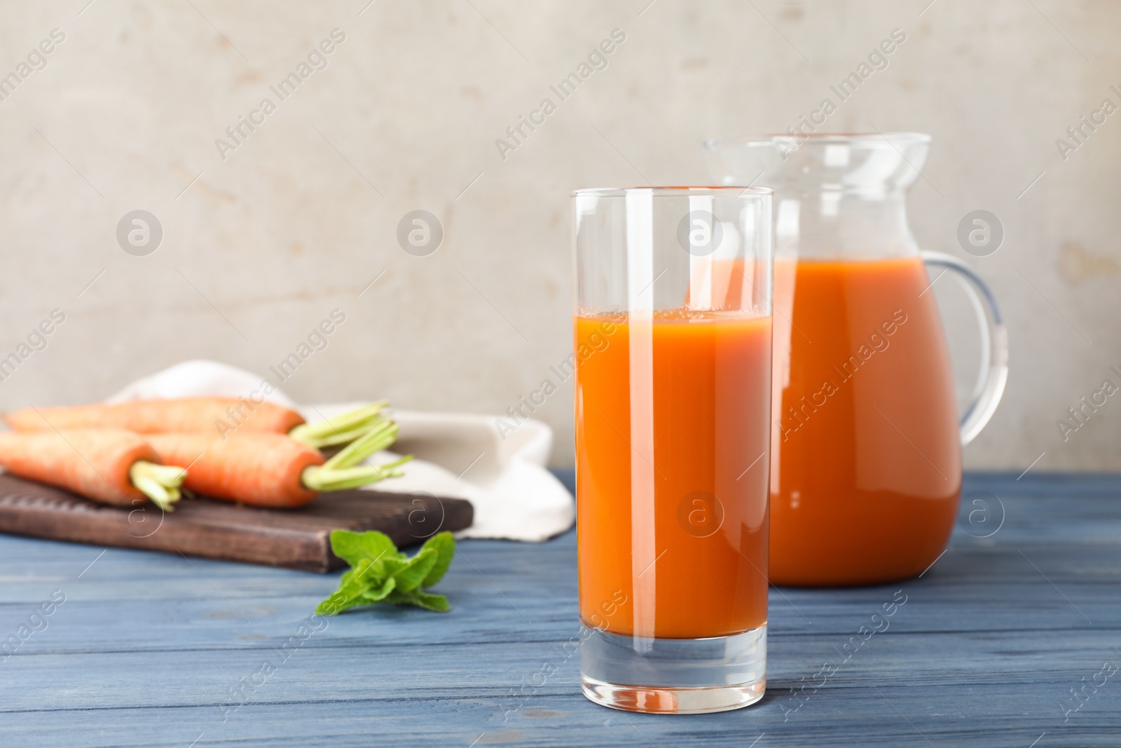 Photo of Glass and jug of carrot drink on table against light background, space for text