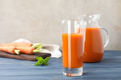 Photo of Glass and jug of carrot drink on table against light background, space for text