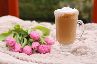 Photo of Glass of delicious cocoa and pink tulips on light blanket at terrace, space for text