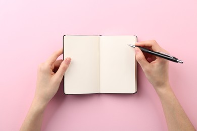 Photo of Woman writing in notebook on pink background, top view