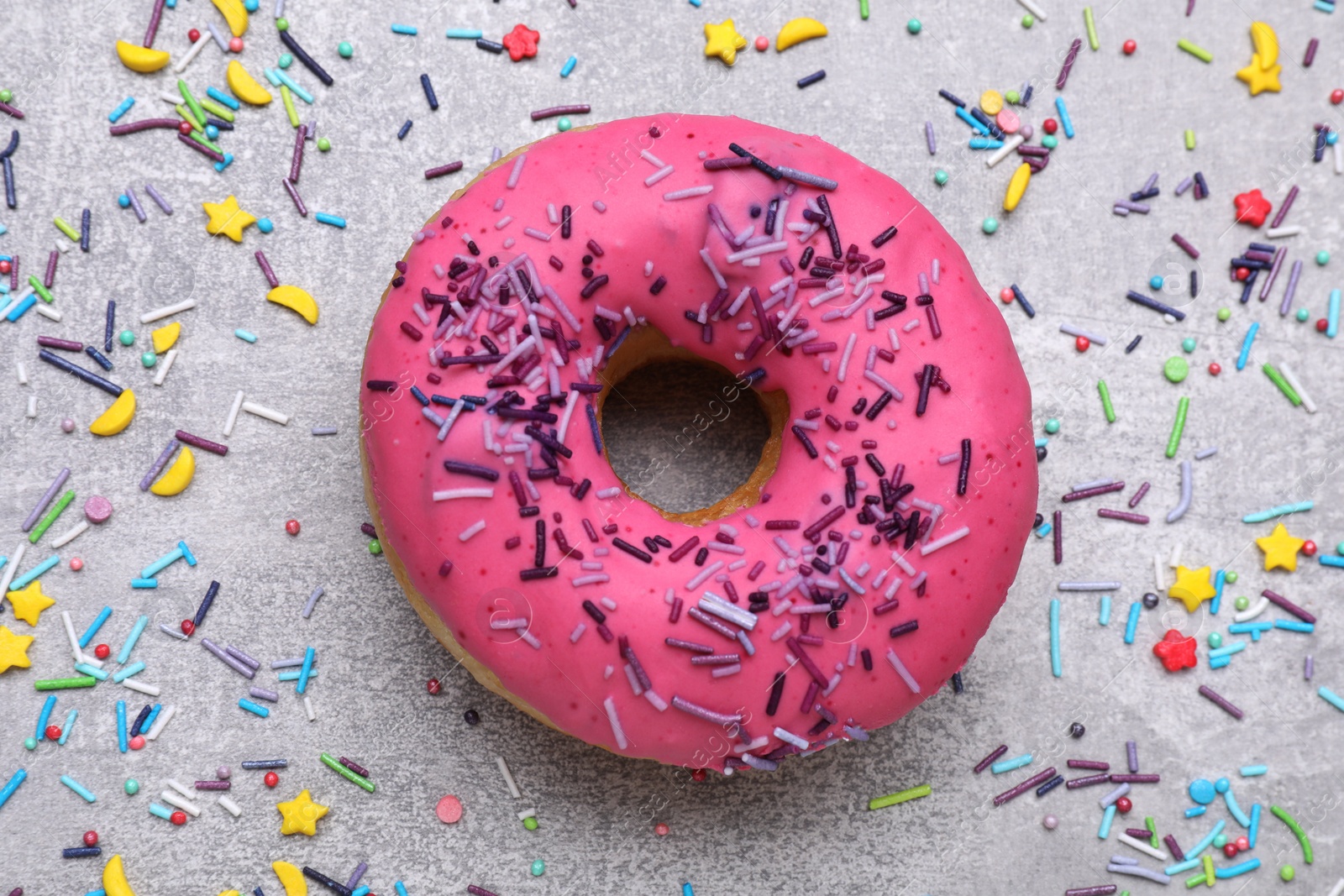 Photo of Sweet glazed donut decorated with sprinkles on light grey table, flat lay. Tasty confectionery