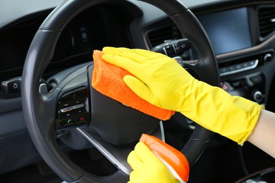 Woman cleaning steering wheel with rag in car, closeup