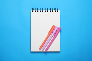 Open notebook and colorful markers on light blue background, top view