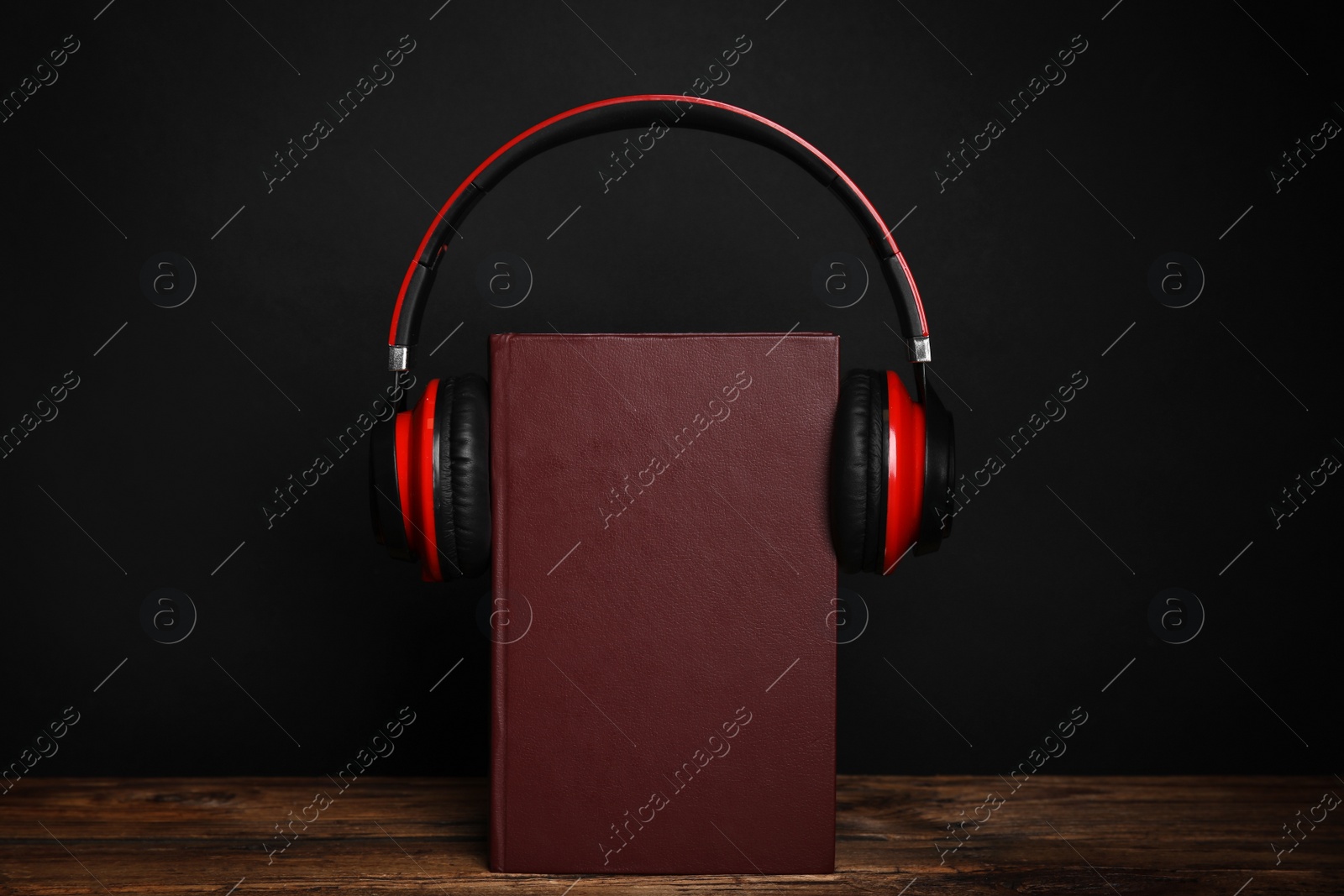 Photo of Book and modern headphones on wooden table against black background