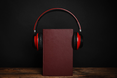 Book and modern headphones on wooden table against black background