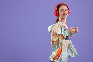 Young woman in sportswear and headphones on violet background, space for text