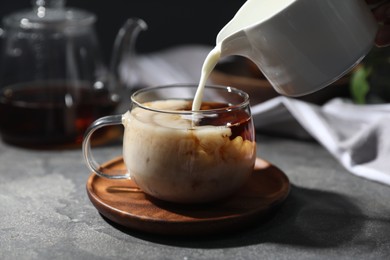 Photo of Pouring milk into cup of tea on grey table, closeup