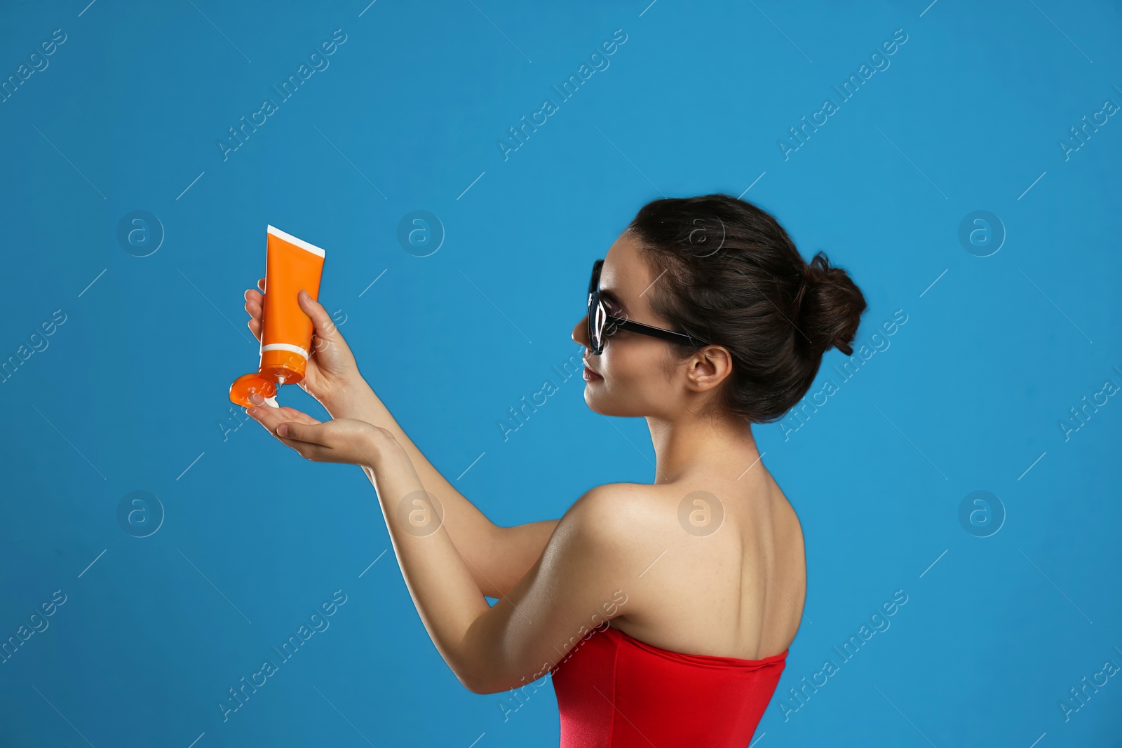 Photo of Young woman applying sun protection cream on dark blue background