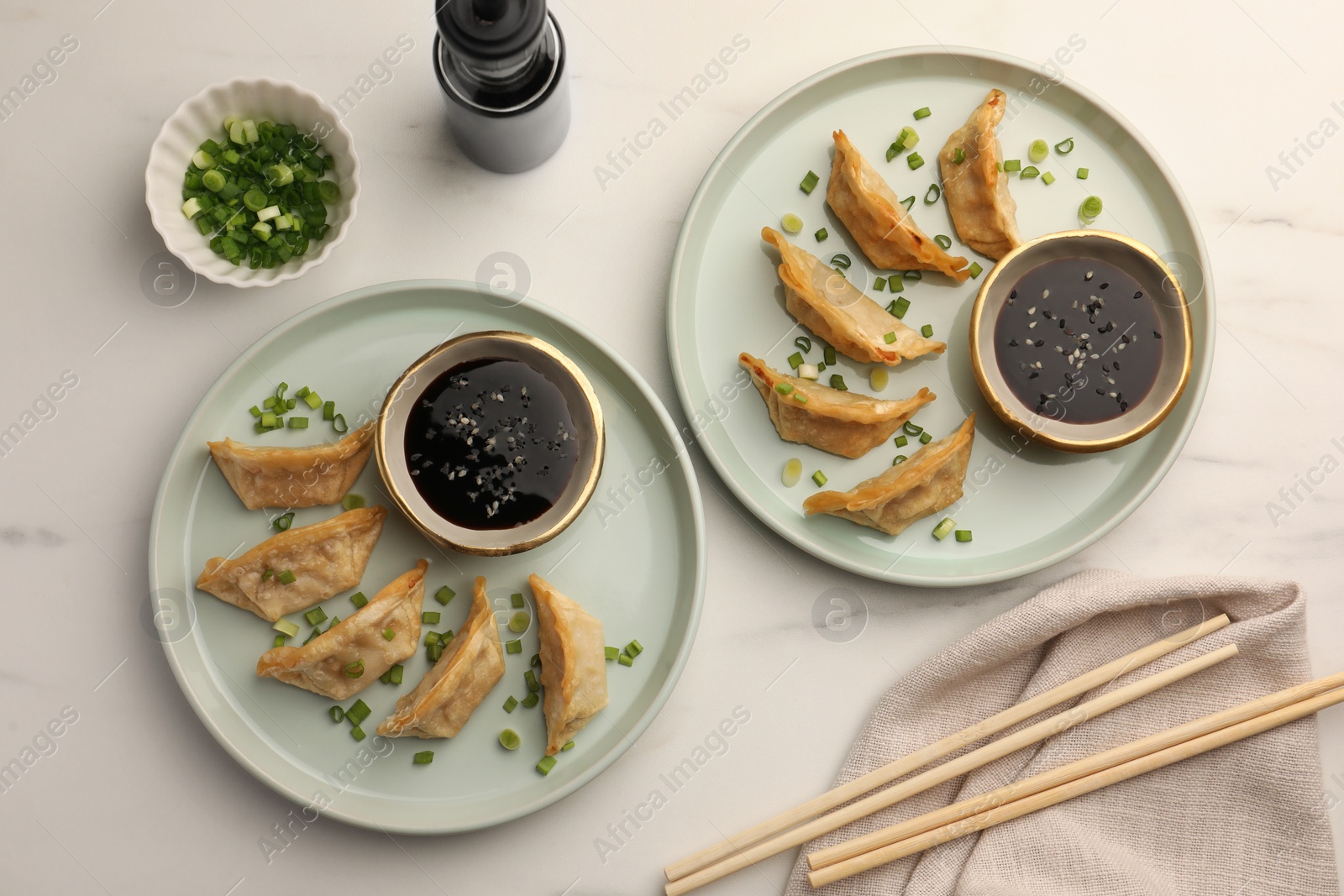 Photo of Delicious gyoza (asian dumplings) with soy sauce, green onions and chopsticks on white table, flat lay