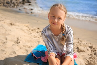 Little girl sitting on sandy beach near sea