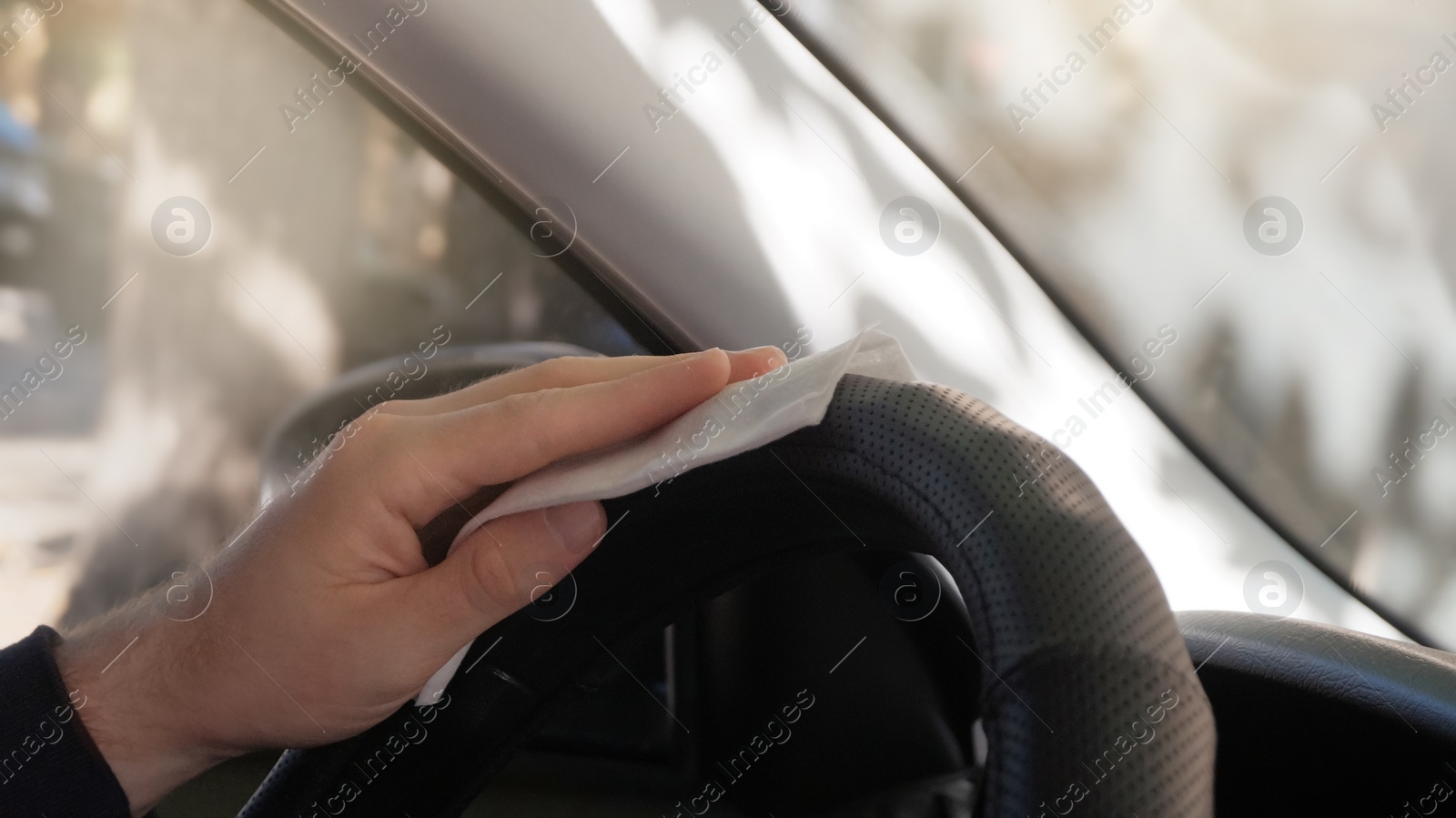 Photo of Man cleaning steering wheel with wet wipe in car, closeup. Protective measures