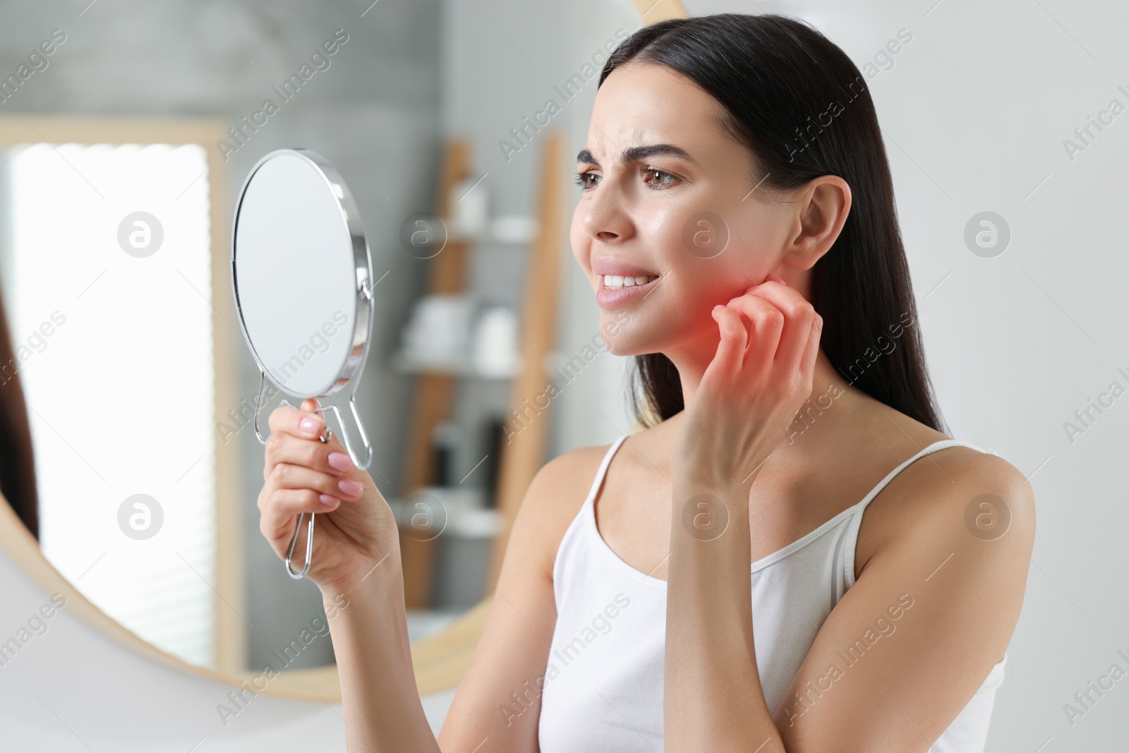 Photo of Suffering from allergy. Young woman looking in mirror and scratching her face indoors