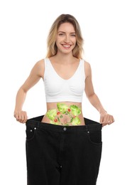 Image of Slim young woman wearing oversized jeans and images of vegetables on her belly against white background. Healthy eating