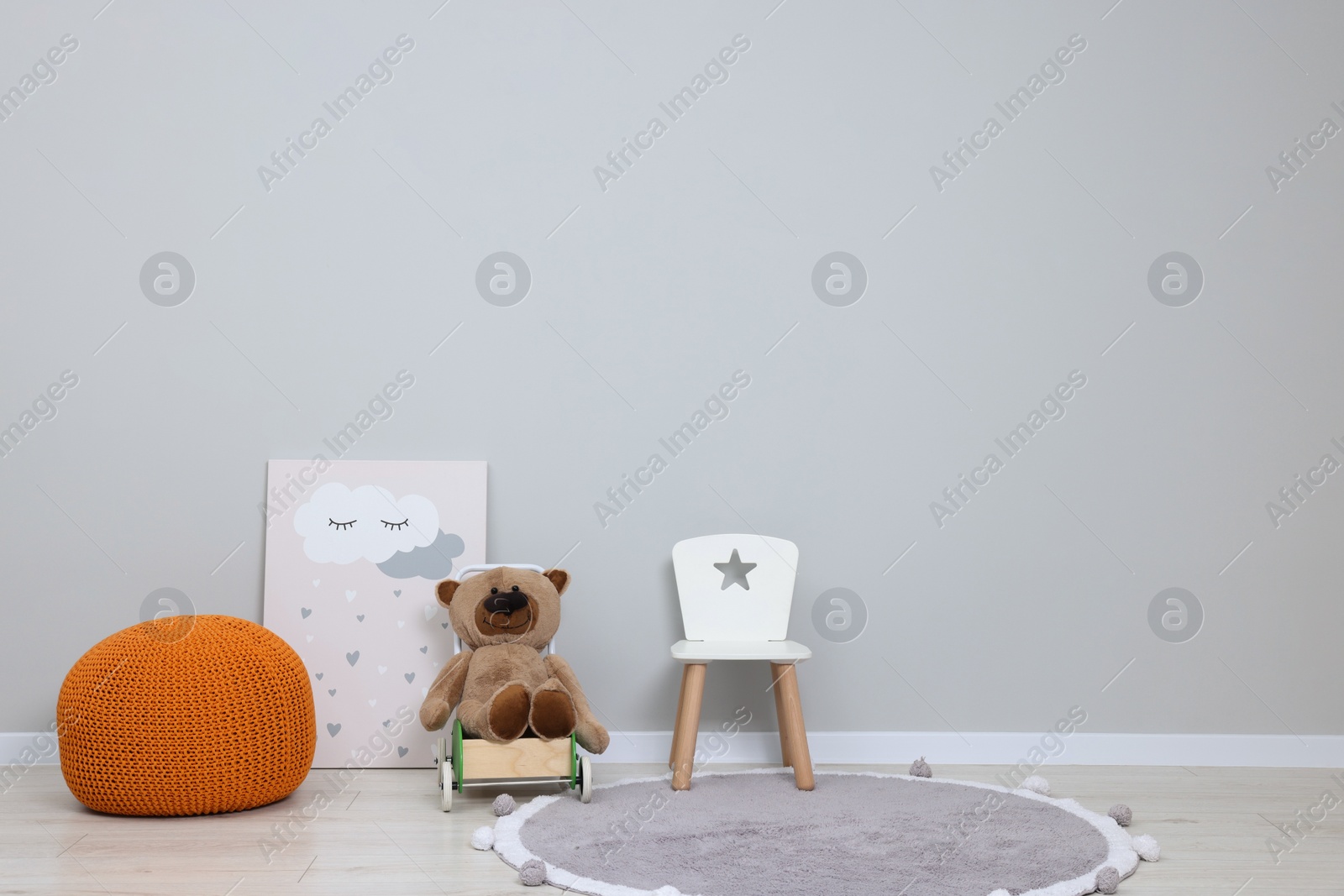 Photo of Kindergarten interior. Small chair, toy, ottoman and picture near grey wall, space for text