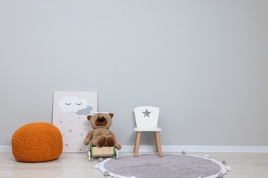 Photo of Kindergarten interior. Small chair, toy, ottoman and picture near grey wall, space for text