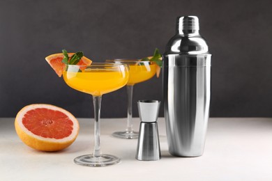 Photo of Metal shaker, delicious cocktail in glasses, jigger and grapefruit on light table