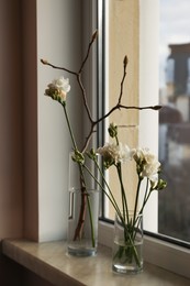 Photo of Different beautiful spring flowers and branches on windowsill indoors