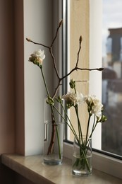 Different beautiful spring flowers and branches on windowsill indoors