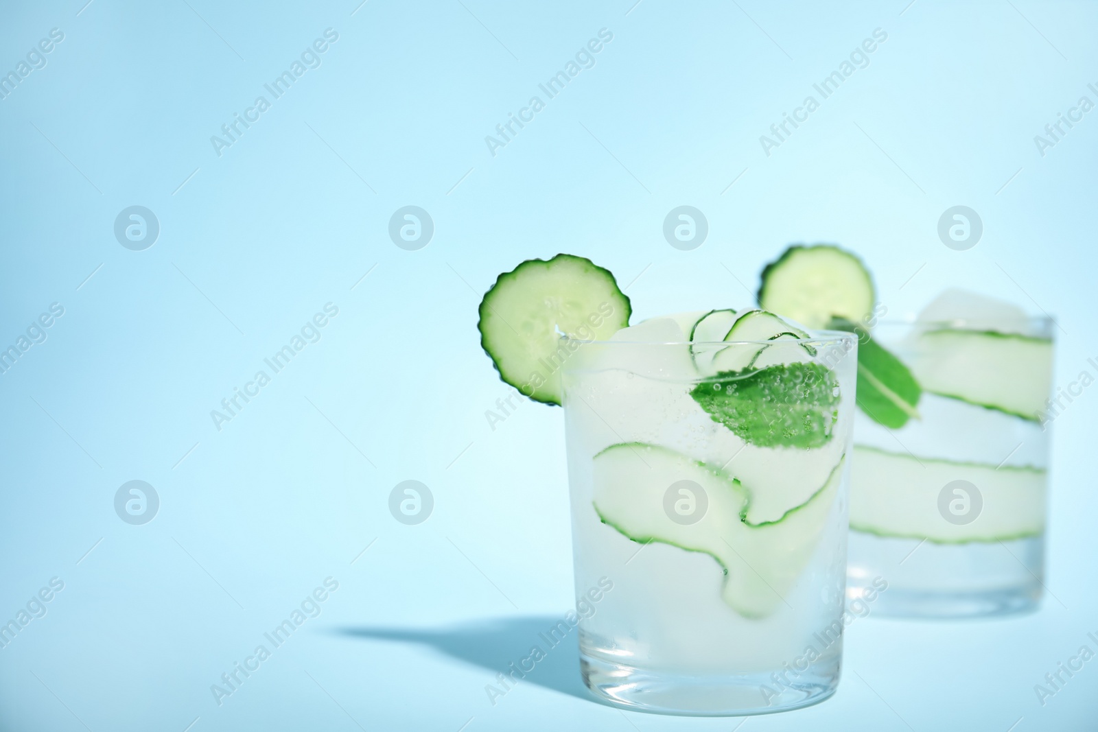 Photo of Tasty fresh cucumber water with mint on light blue background, space for text