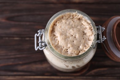 Photo of Sourdough starter in glass jar on wooden table, top view. Space for text