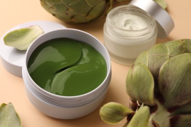 Photo of Package of under eye patches, cream and artichokes on beige background, closeup. Cosmetic product