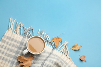 Flat lay composition with coffee and warm plaid on light blue background, space for text