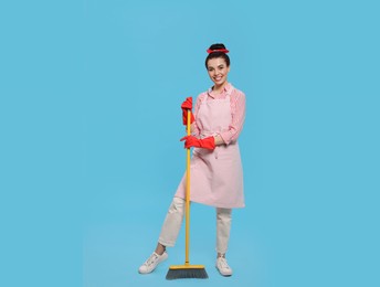 Photo of Young housewife with broom on light blue background, space for text