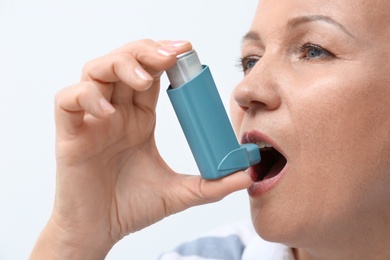 Photo of Woman using asthma inhaler on white background, closeup