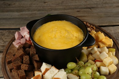 Fondue pot with melted cheese and different products on wooden table, closeup