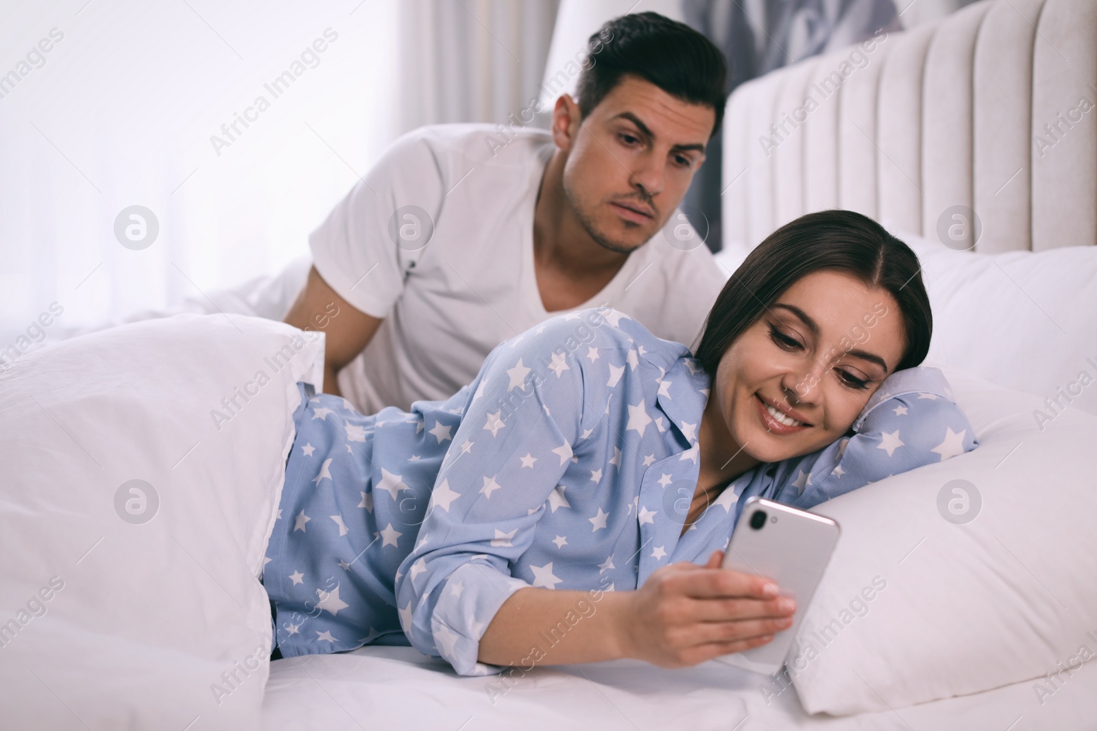 Photo of Distrustful man peering into girlfriend's smartphone at home. Jealousy in relationship