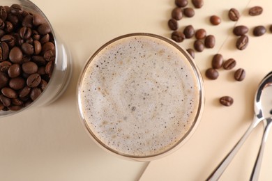 Photo of Refreshing iced coffee with milk in glass, beans and spoons on beige table, flat lay