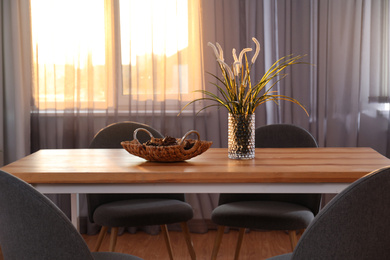 Vase on wooden table near window with curtains in room