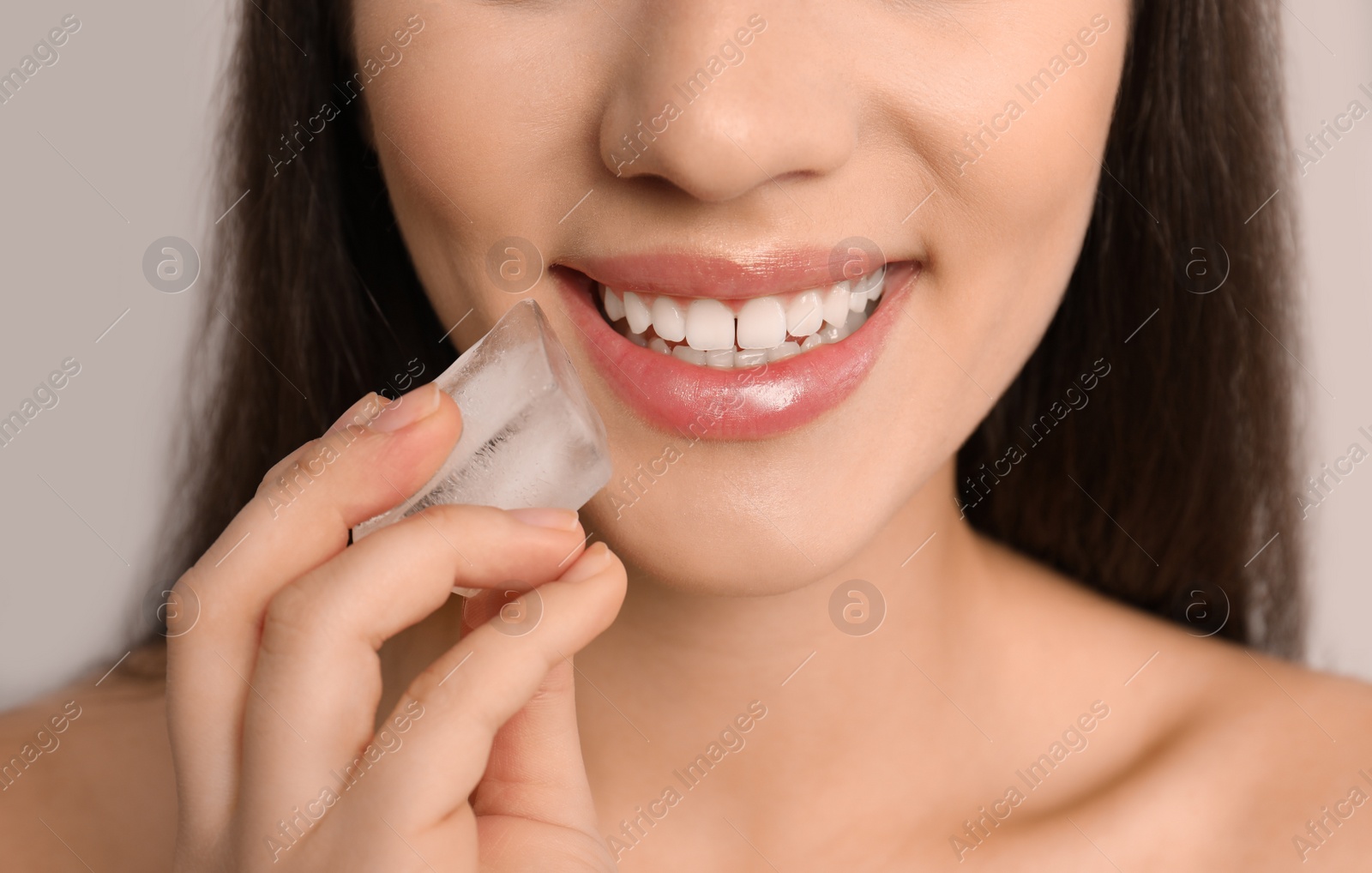 Photo of Young woman with ice cube on light background, closeup. Skin care