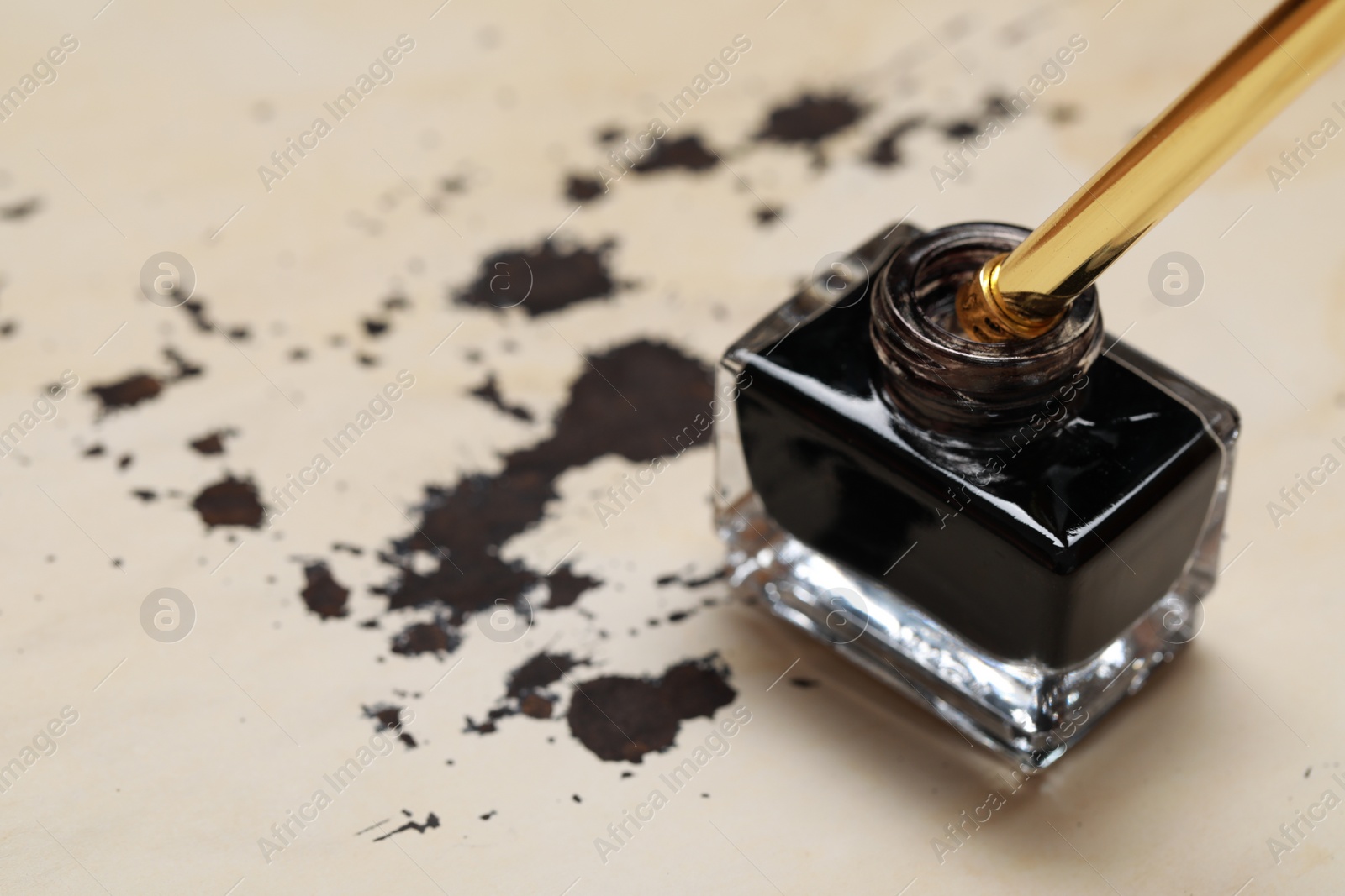 Photo of Inkwell with fountain pen on vintage parchment with ink stains, closeup