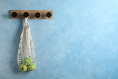 Photo of Wooden rack with delicious apples in mesh bag on light blue wall. Space for text