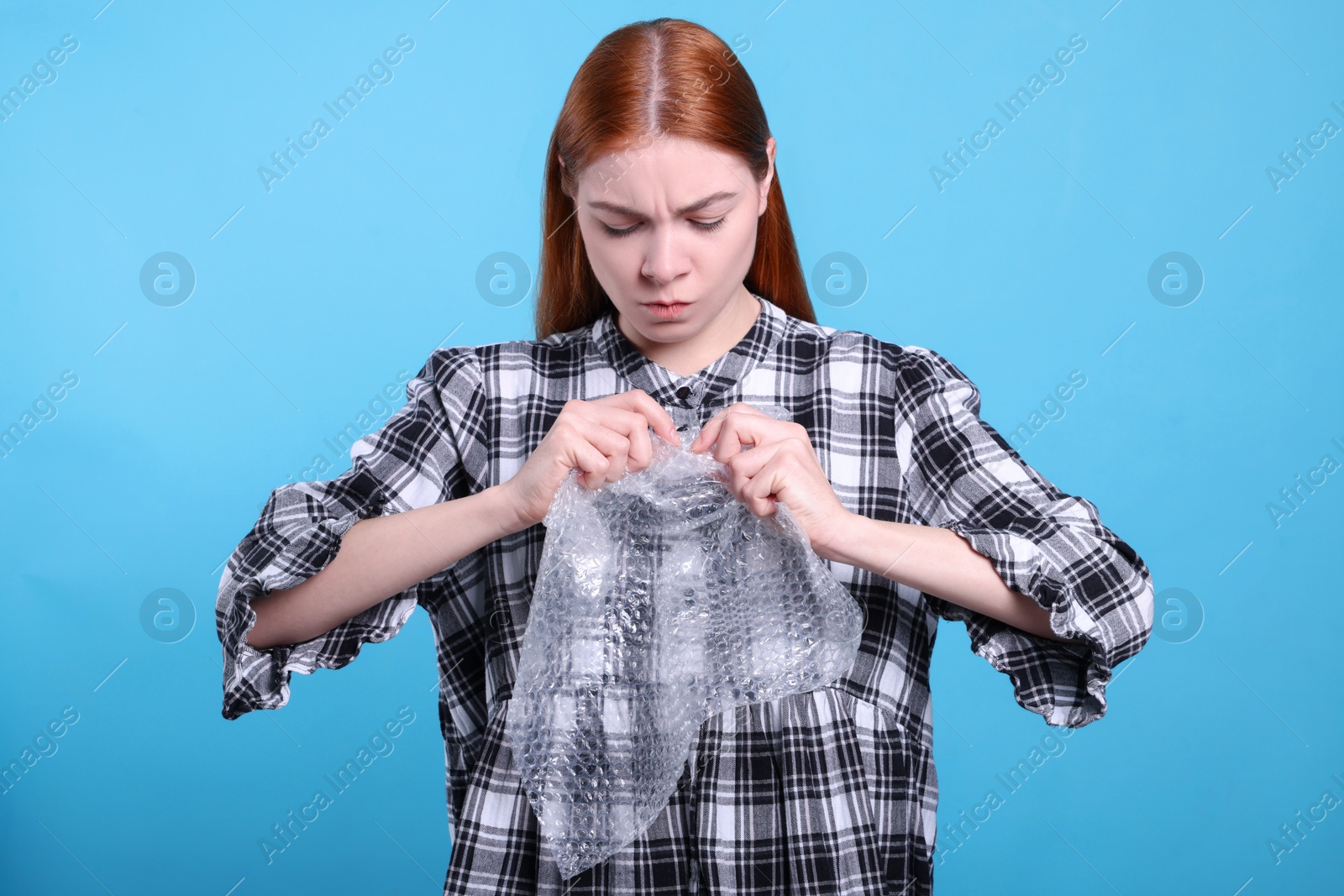 Photo of Angry woman popping bubble wrap on turquoise background. Stress relief