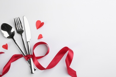 Photo of Cutlery set and red ribbon on white background, flat lay with space for text. Valentine's Day dinner
