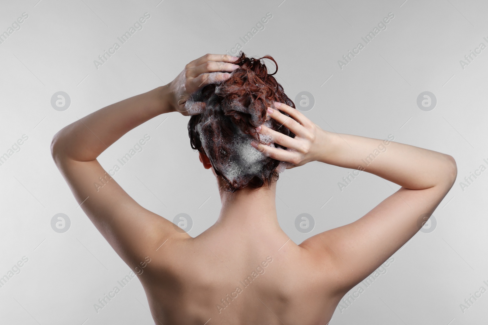 Photo of Young woman washing her hair with shampoo on light grey background, back view