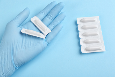 Photo of Woman holding suppositories on light blue background, top view. Hemorrhoid treatment
