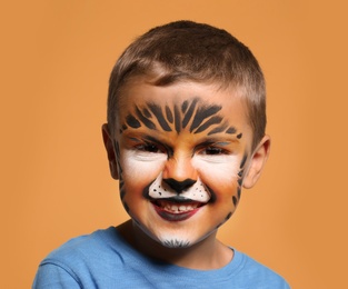 Photo of Cute little boy with face painting on orange background