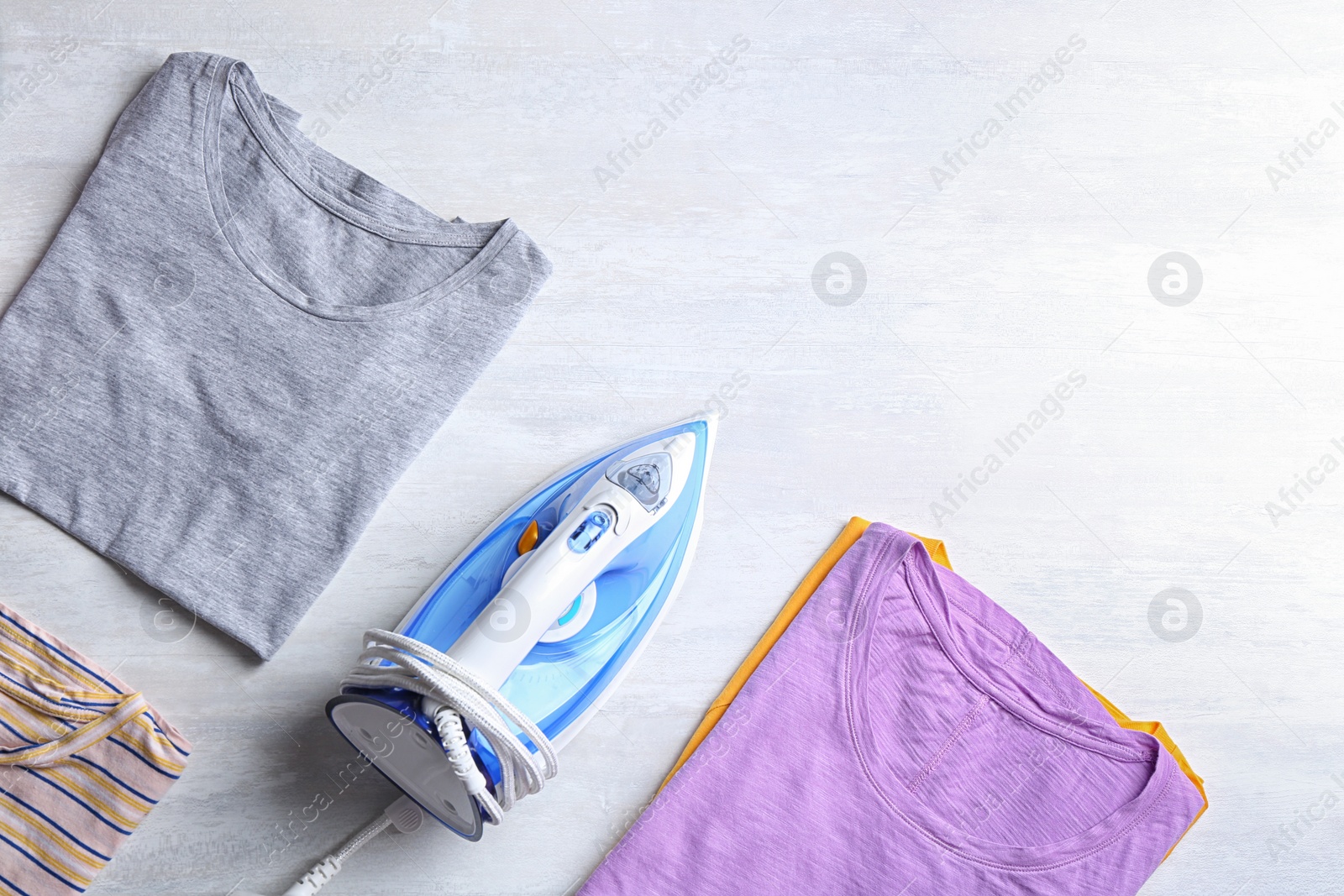 Photo of Flat lay composition with folded clothes and modern iron on light table. Space for text