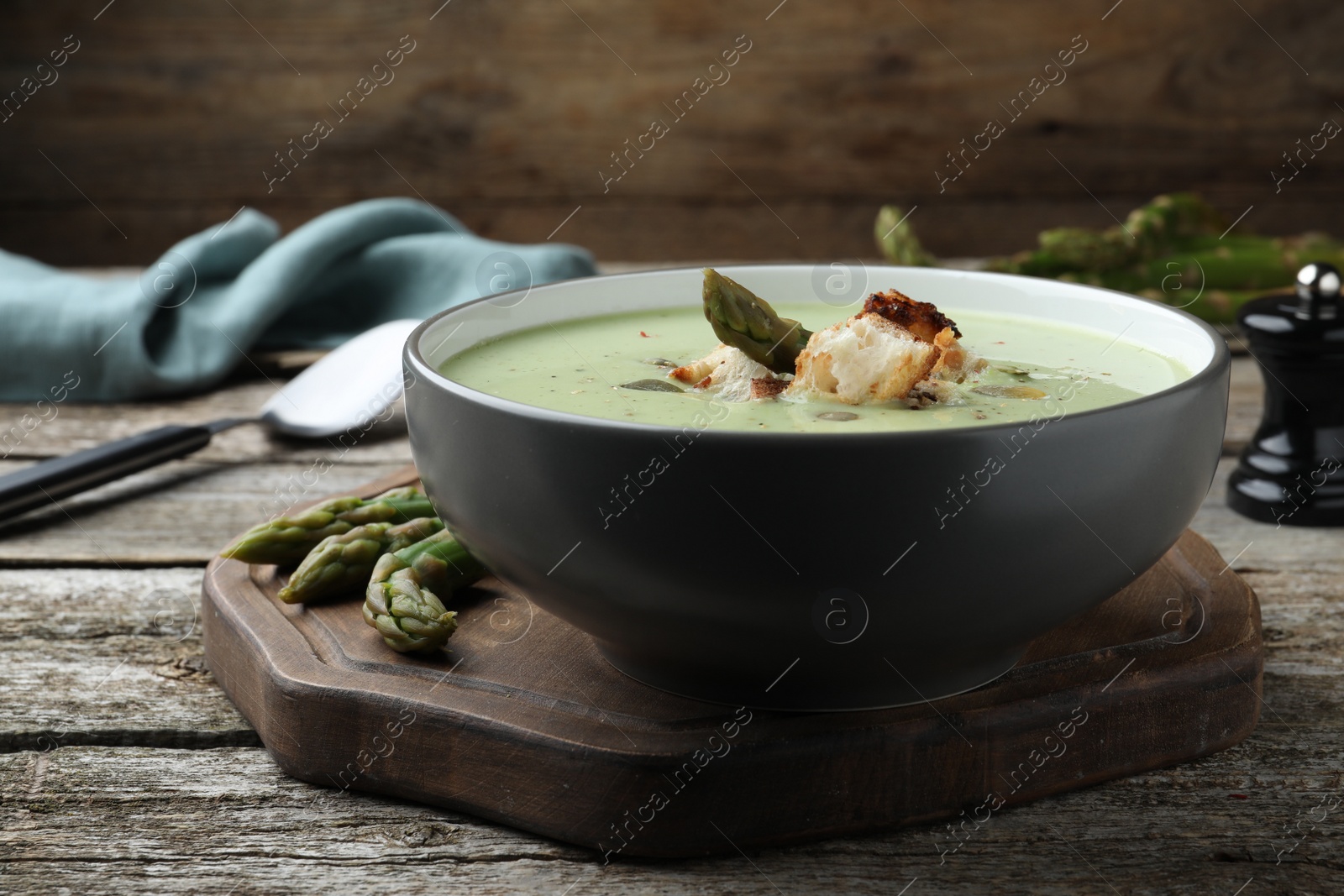 Photo of Bowl of delicious asparagus soup on wooden table