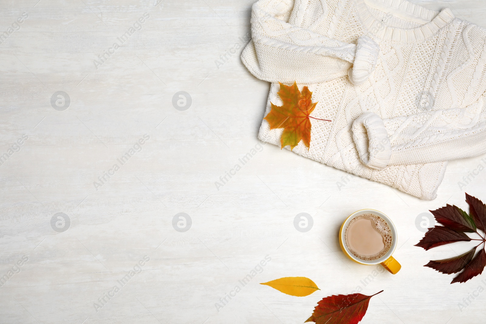 Photo of Stylish clothing, autumn leaves and cup of coffee on white wooden background, flat lay with space for text