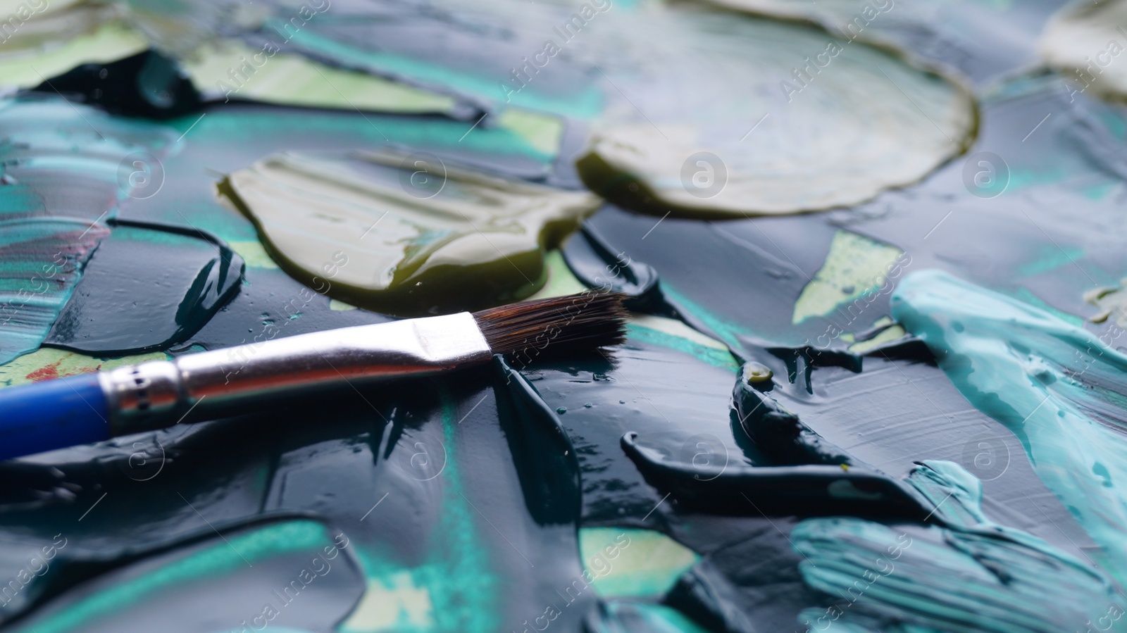 Photo of Brush on artist's palette with mixed paints, closeup