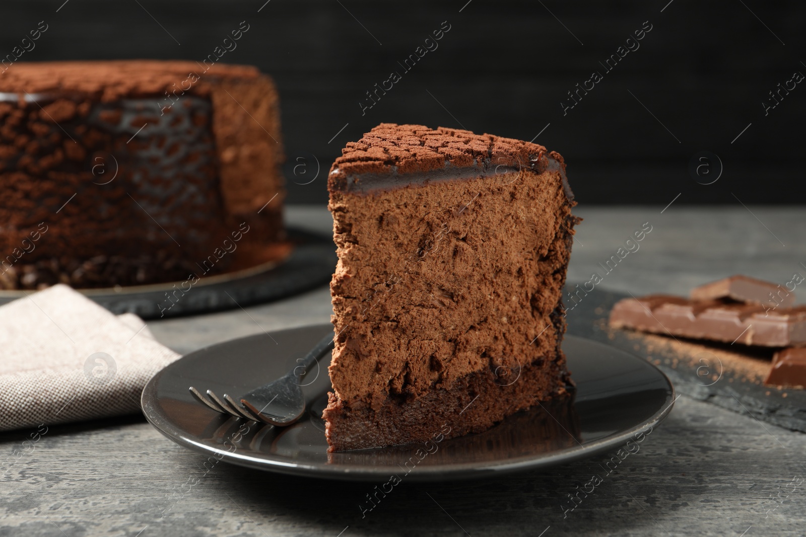 Photo of Piece of delicious chocolate truffle cake and fork on grey textured table, closeup