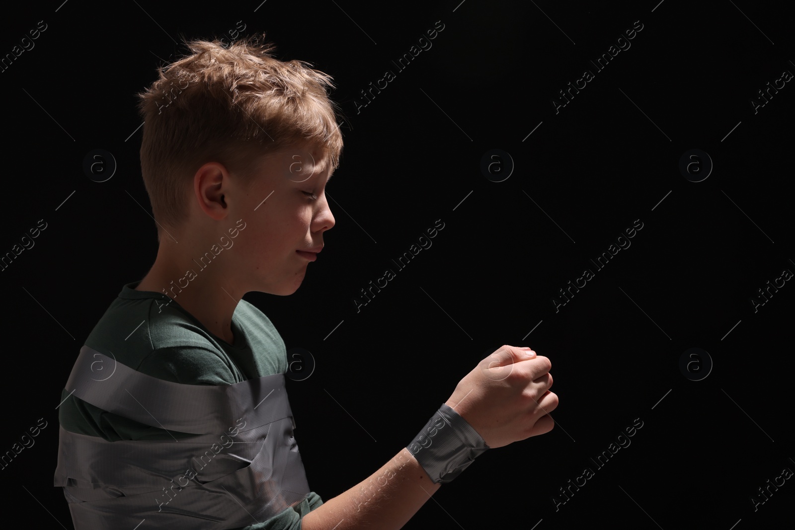 Photo of Little boy tied up and taken hostage on dark background. Space for text