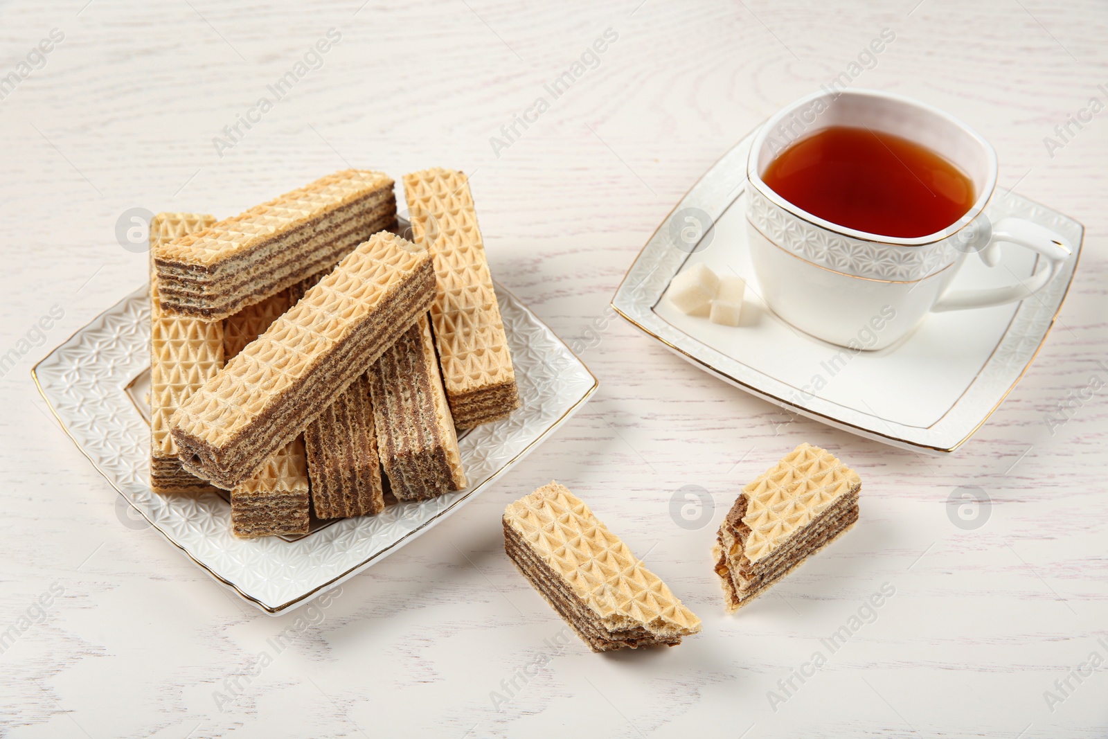 Photo of Plate of delicious wafers with cup of tea on white wooden background